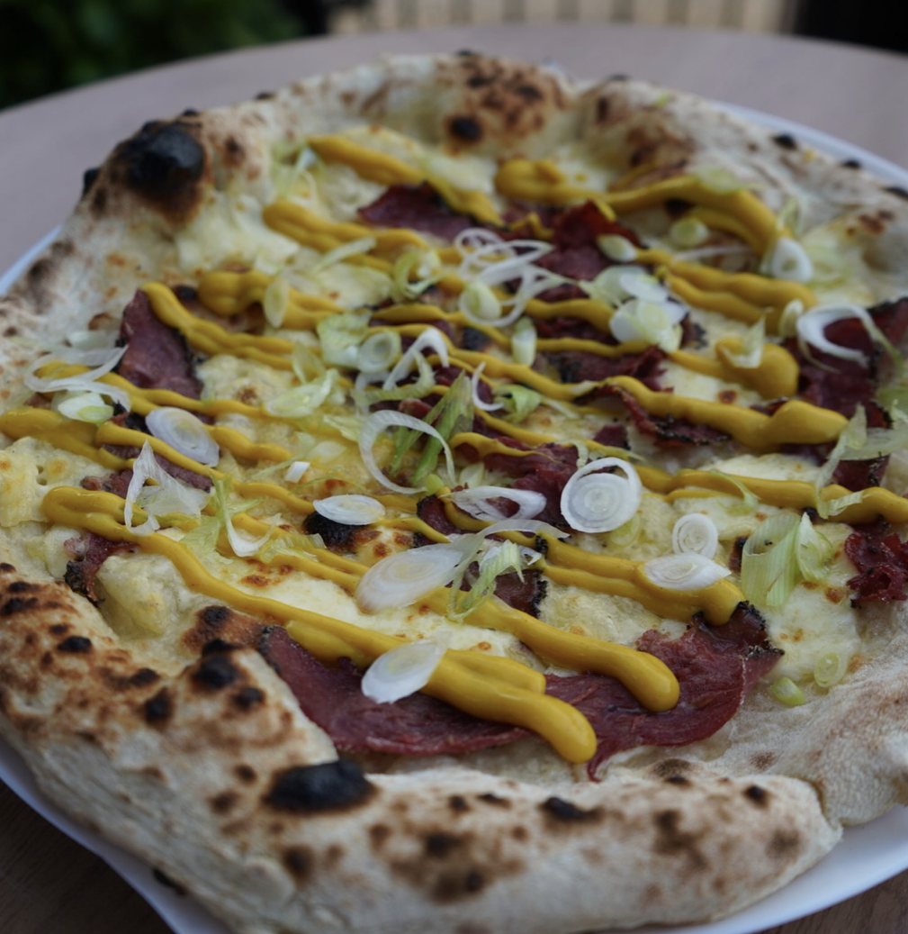 Pizza topped with pastrami, mustard and spring onion